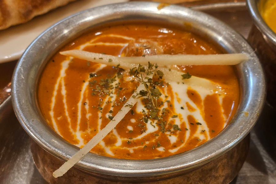 銀の皿に入ったオレンジ色のバターチキンカレー