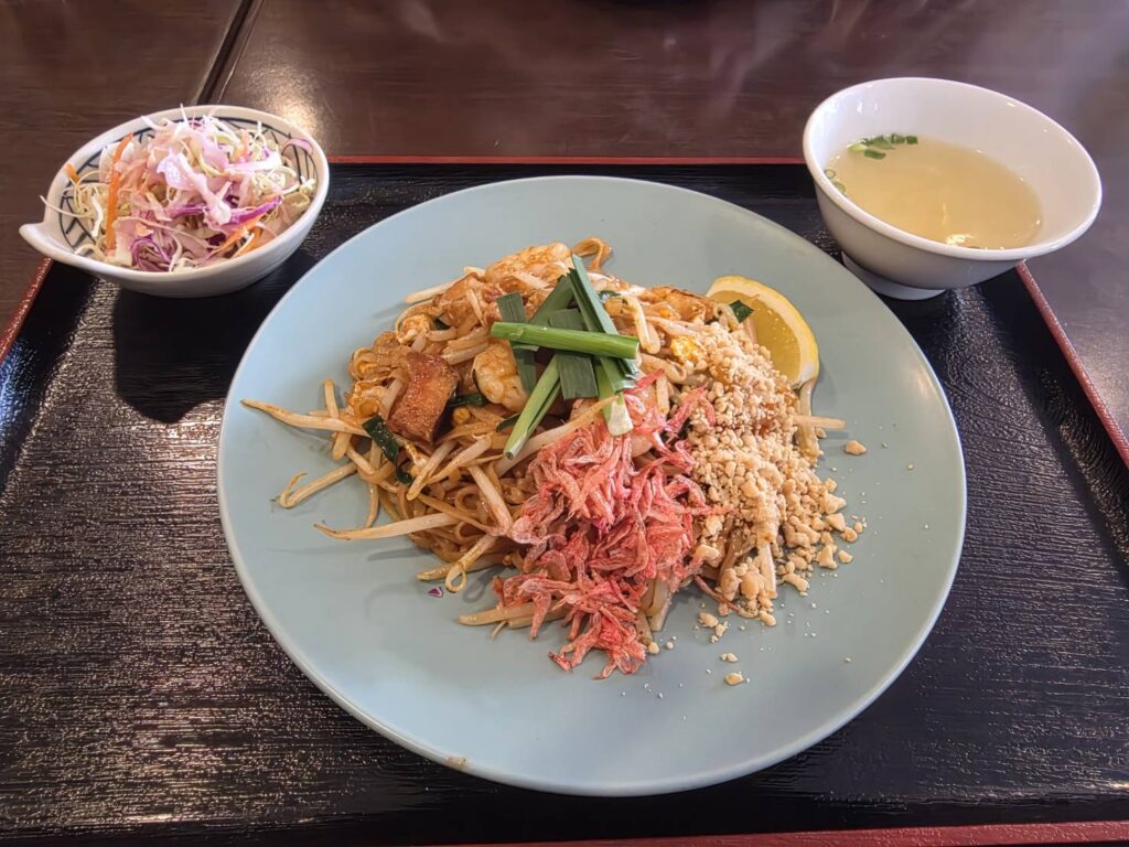 青い皿に乗ったパッタイが黒いトレーに乗っている