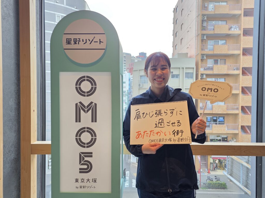 縦長の看板の横でスケッチブックを持って立つ女性